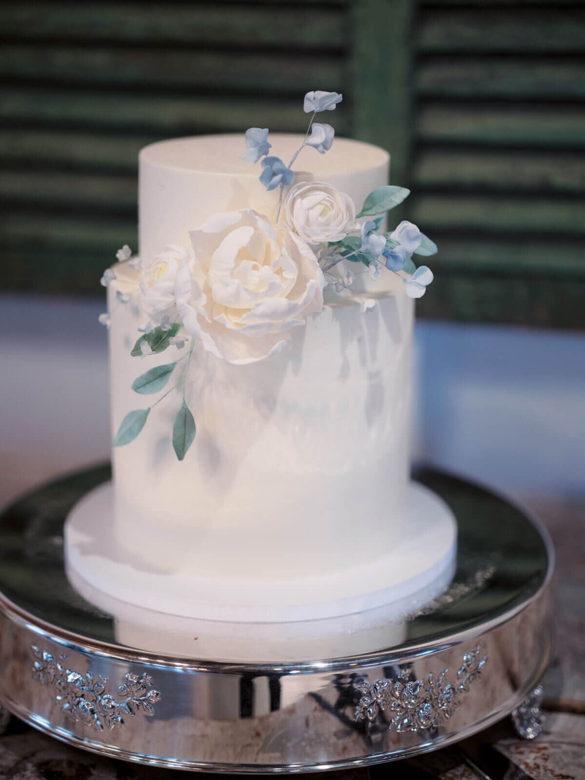 A simple white wedding cake with a big white flower and green leaves as an accent at Lion Rock Farm, CT. Image by Jenny Fu Studio