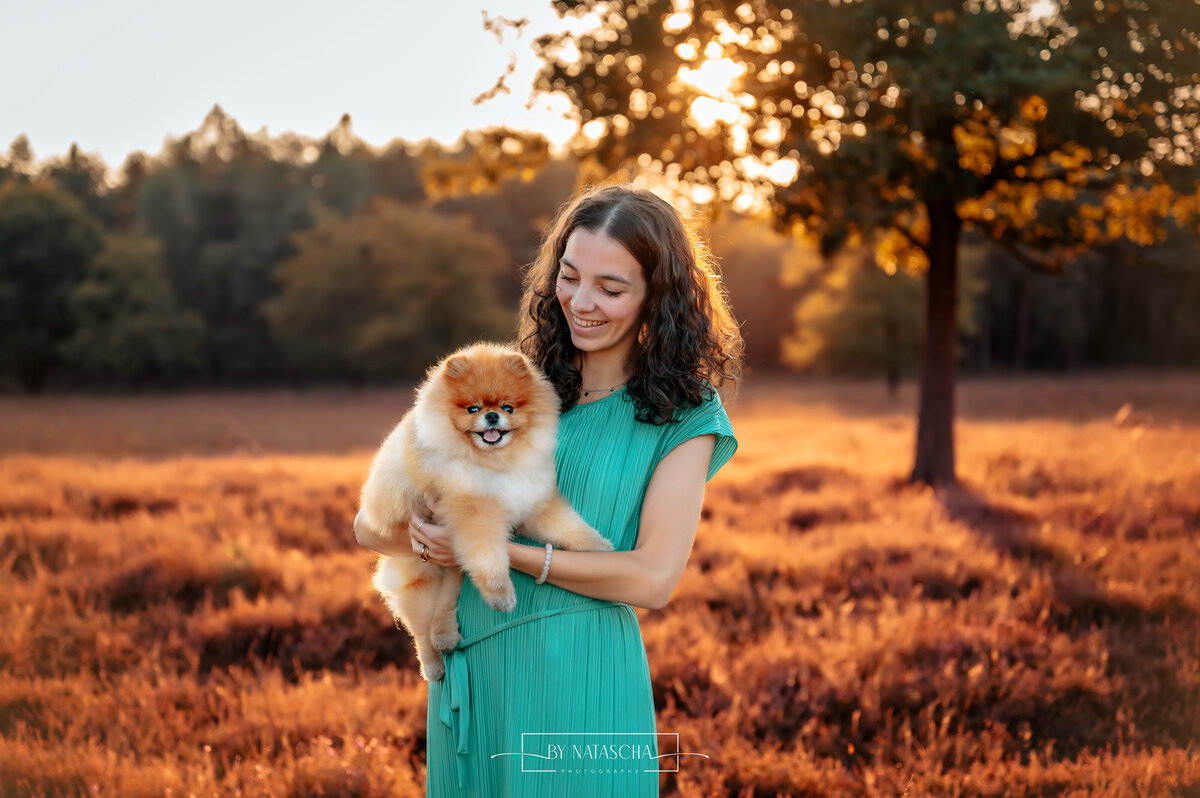 Nienke met haar hondje pomeriaan Buddy in de heide van Herperduin terwijl ze hem vasthoudt en de zon ondergaat