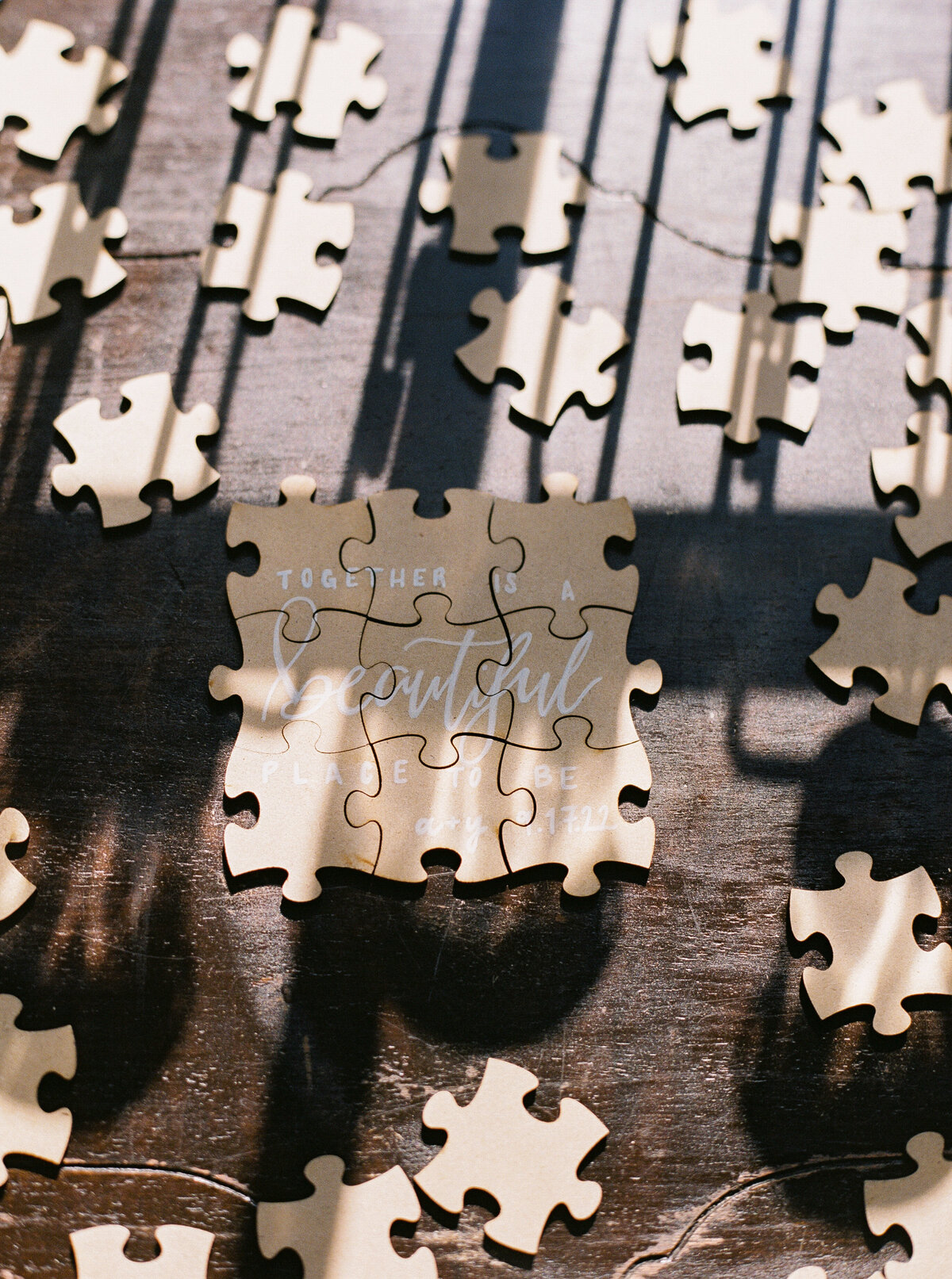Close-up of a wedding guestbook puzzle piece with calligraphy reading “Together is a beautiful place to be,” styled on a wooden table with sunlight and shadows.
