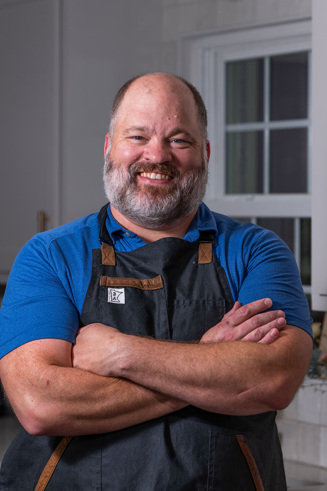 A person in an apron smiling with their arms crossed 