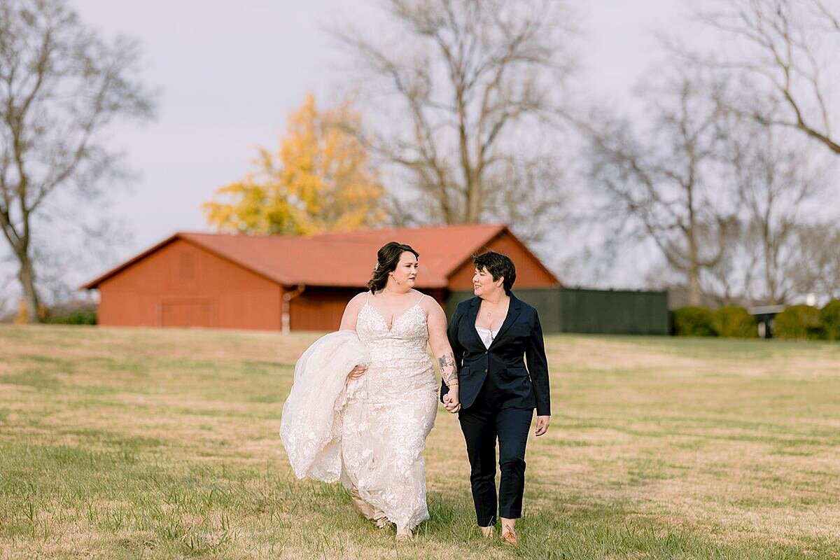 a bride in a wedding dress and a bride in a suit walking in a Tennessee field