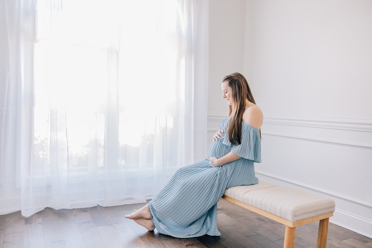pregnant woman sitting on bench next to a window