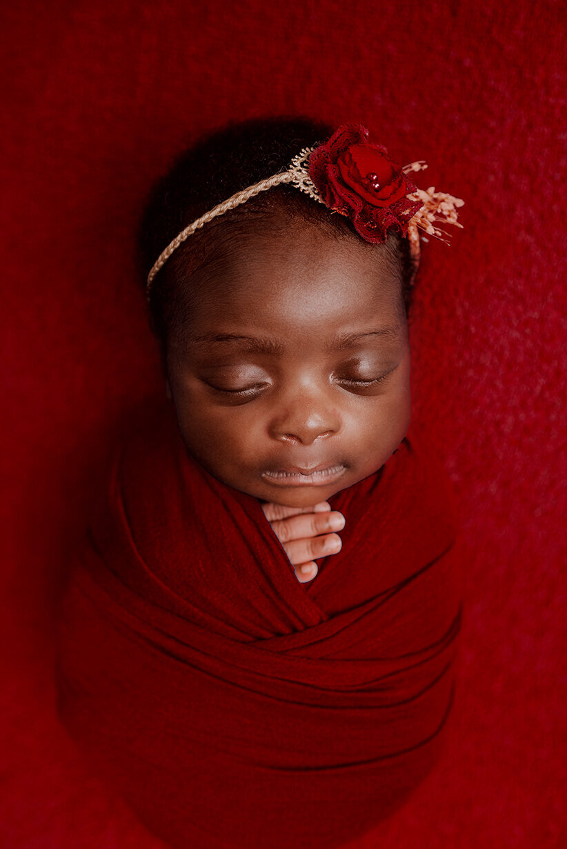 Sleeping baby wrapped in red laying on a red background