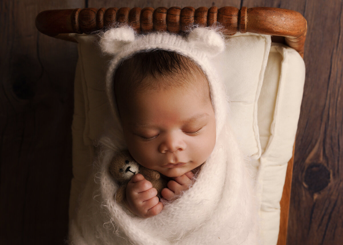 baby boy holding teddy bear in white with teddy bonnet near bellevue