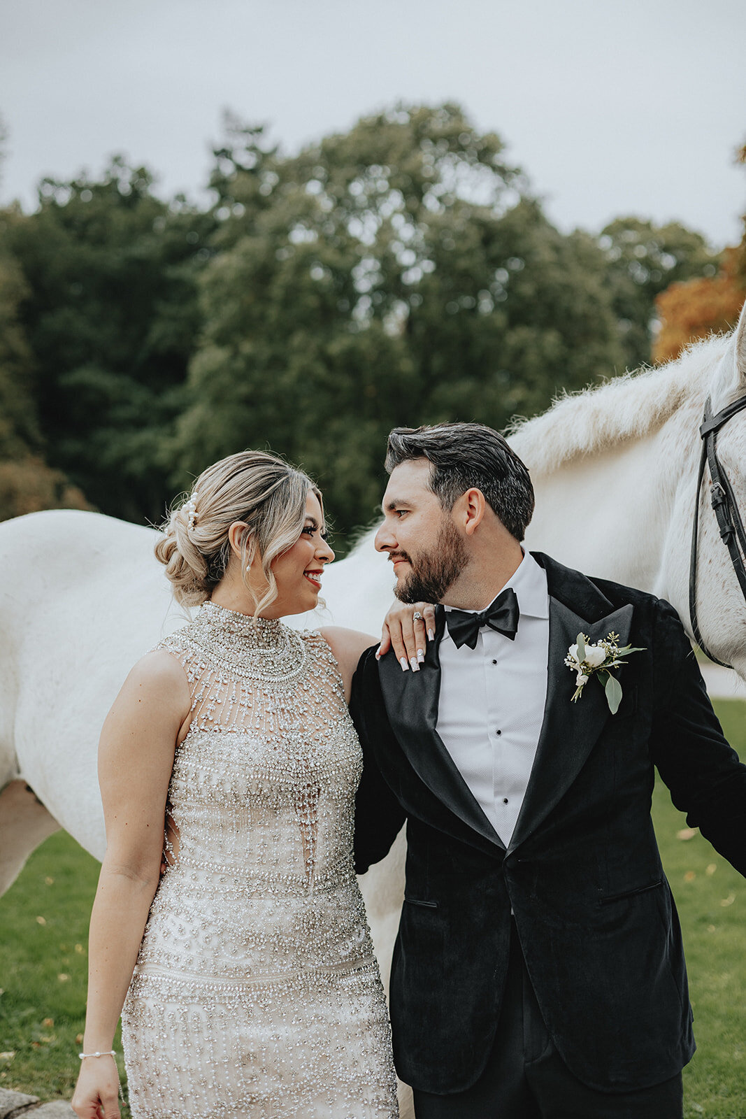 Bride and groom smiling at each other with white horse in back