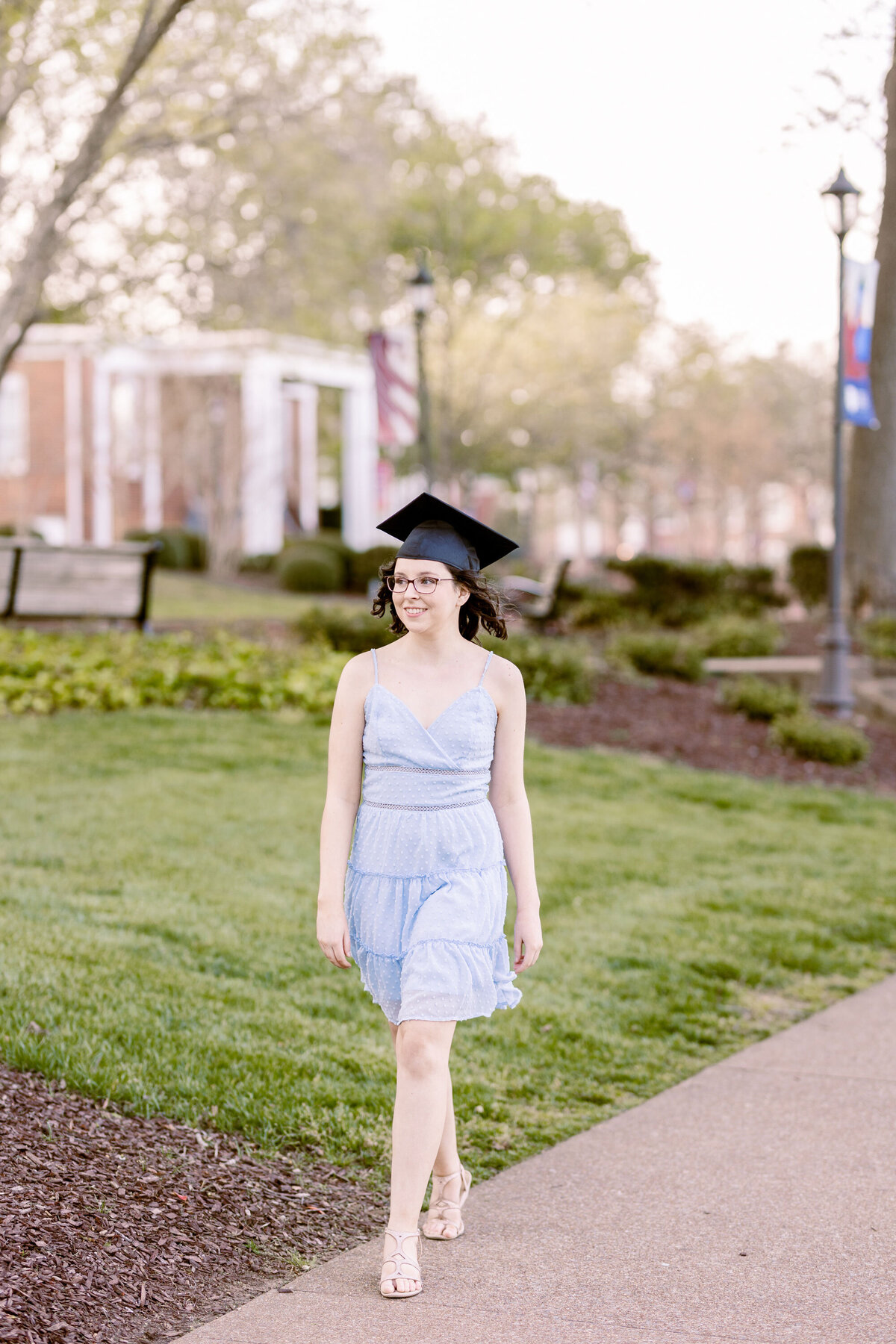college senior wearing a blue dress and cap walking on Lee University's campus