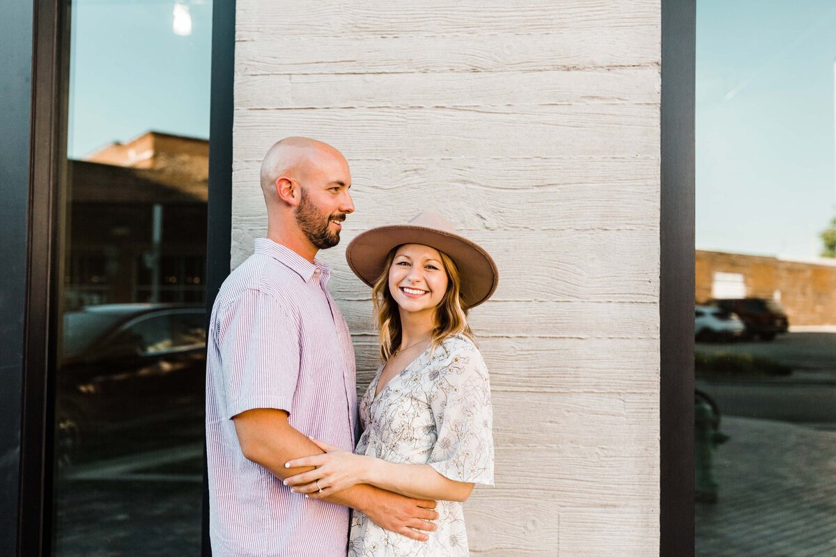 Couple smiling and embracing in front of a light brick wall during a lifestyle photo session in South Bend.