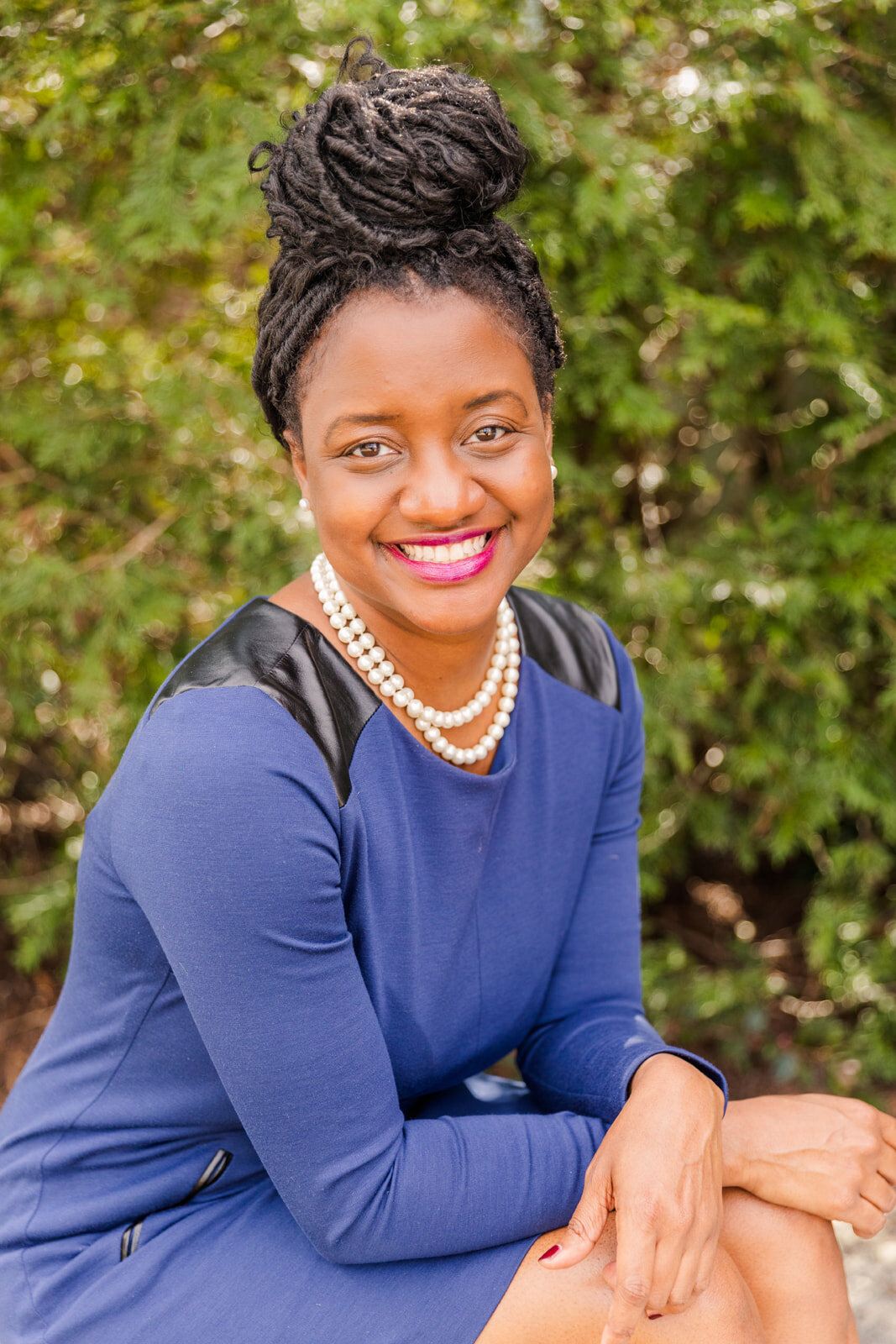 woman in blue business dress sitting and smiling in front of greeneries with Laure Photography branding