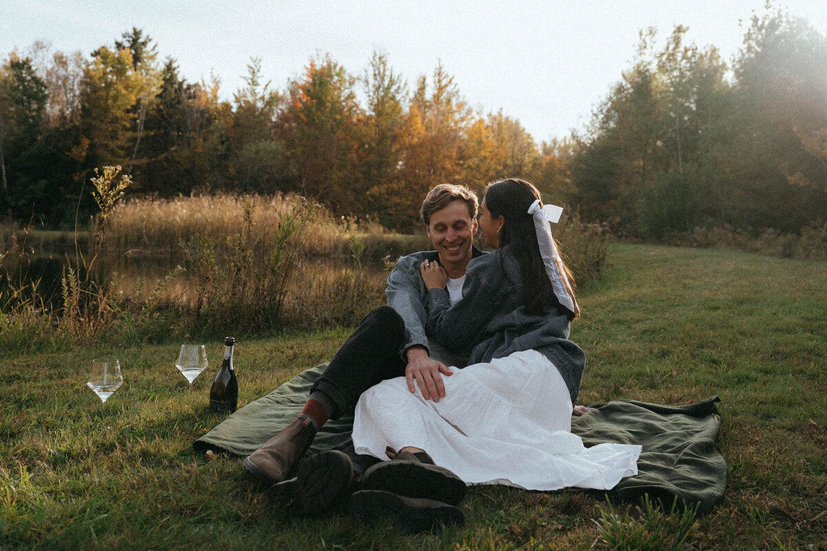 couple sitting in grass with wine during vermont engagement photos, captured by Elsie Goodman, an NYC and destination couples photographer