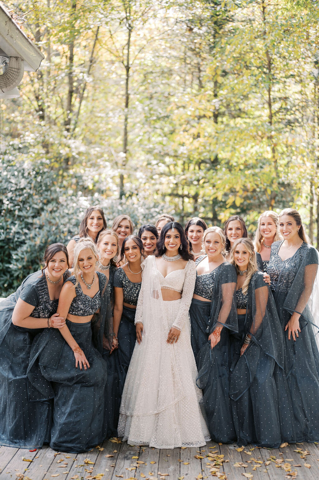 Bride surrounded by bridesmaids wearing matching dark blue sparkling lehengas outdoors.