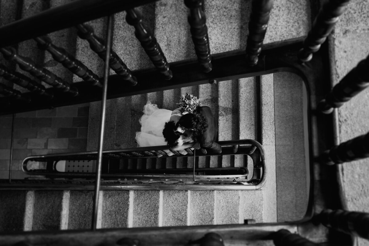 Black and white shot of bride descending staircase with bouquet
