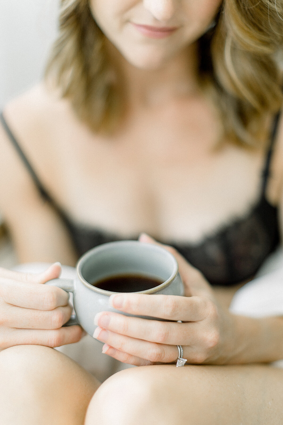 Close up detail boudoir portrait of a woman holding a cup of coffee while she is dressed in a set of black lace lingerie.