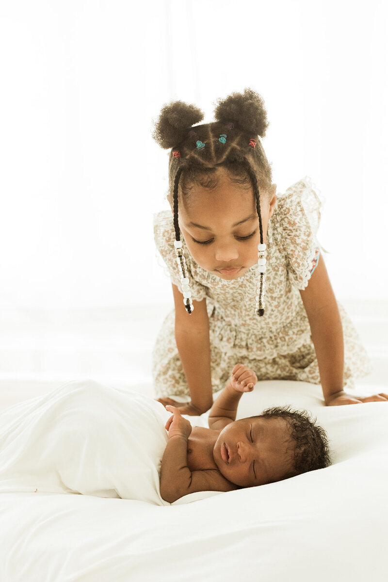 Big sister checks on her newborn brother to make sure he is still sleeping