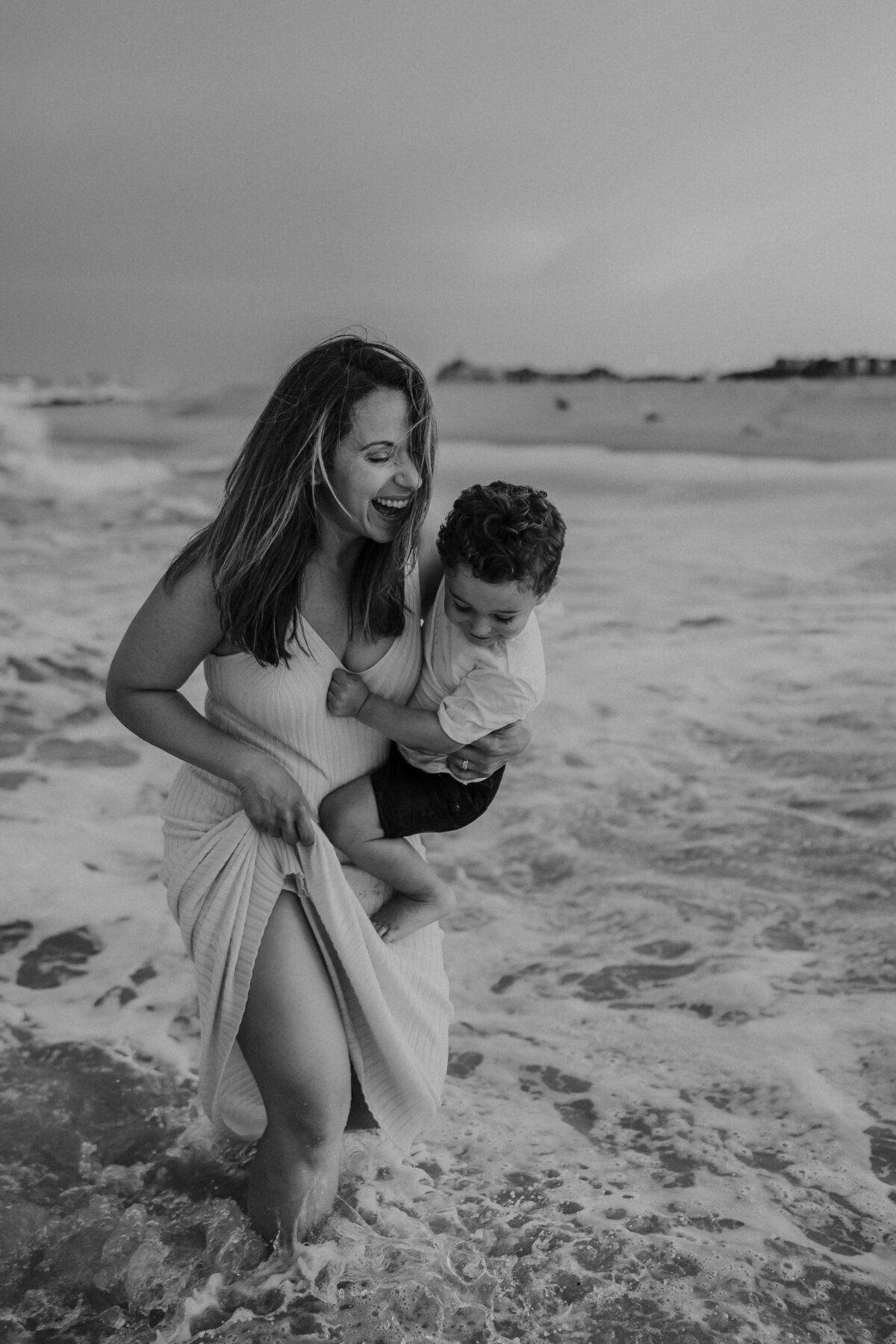 Mom splashing in the ocean with son and laughing