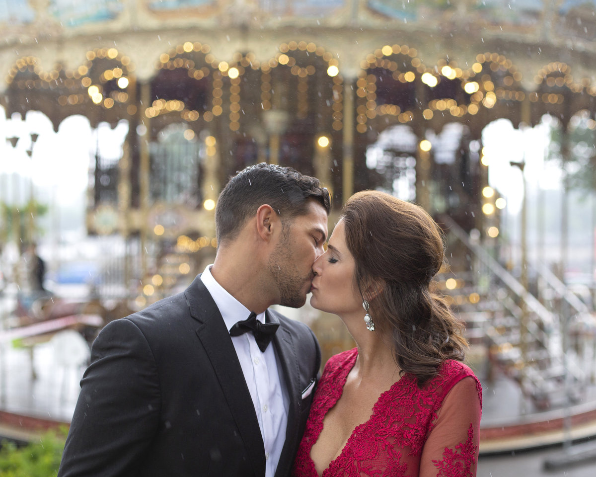 Dressed up couple kisses in front of carousel in Paris