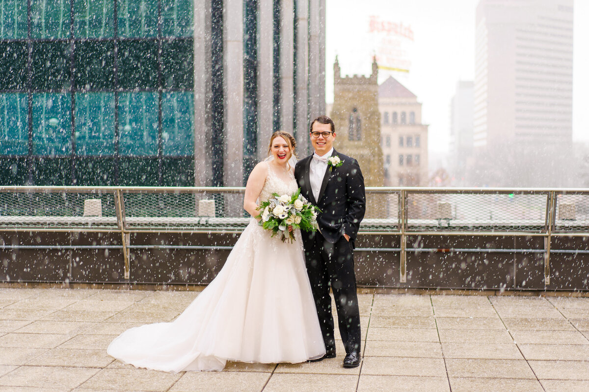 Bride and groom laugh as they're showered with snow on top of a roof in downtown Columbus, Ohio.