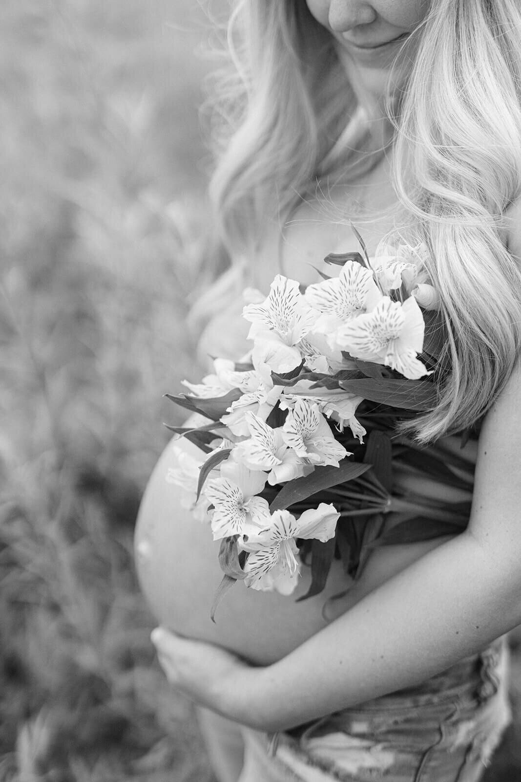 woman holding flowers tucked under her arms holding baby bump