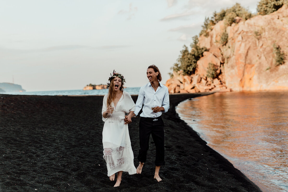 black sand beach elopement with bride and groom walking enjoying champagne