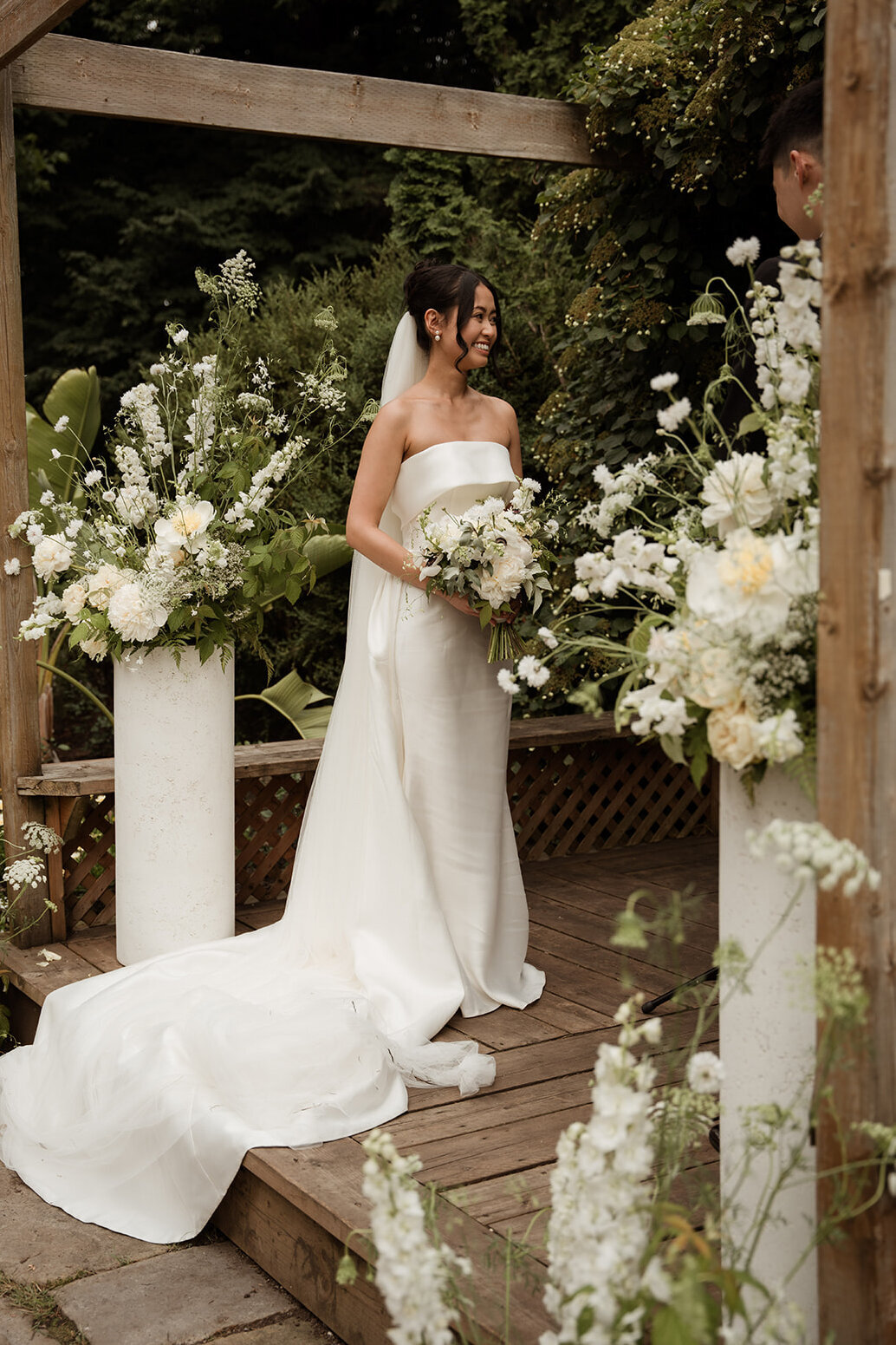 A smiling bride stands between two large floral ceremony arrangements at La Toundra.