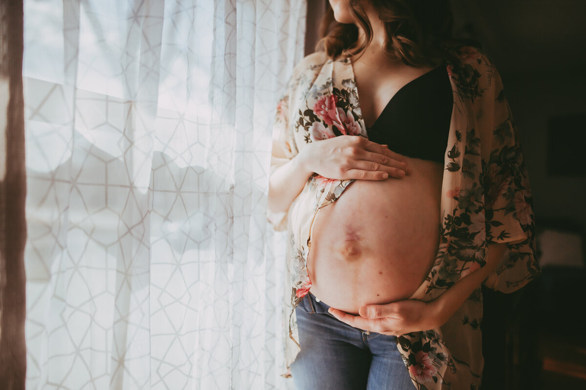 pregnant mom stands near the window