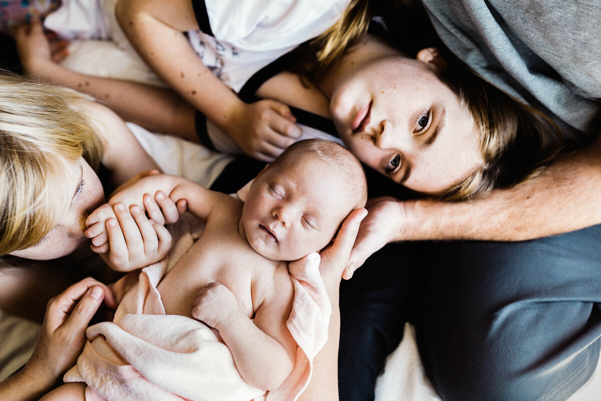 Birds eye view of a young family snuggling bed while cradling newborn baby.