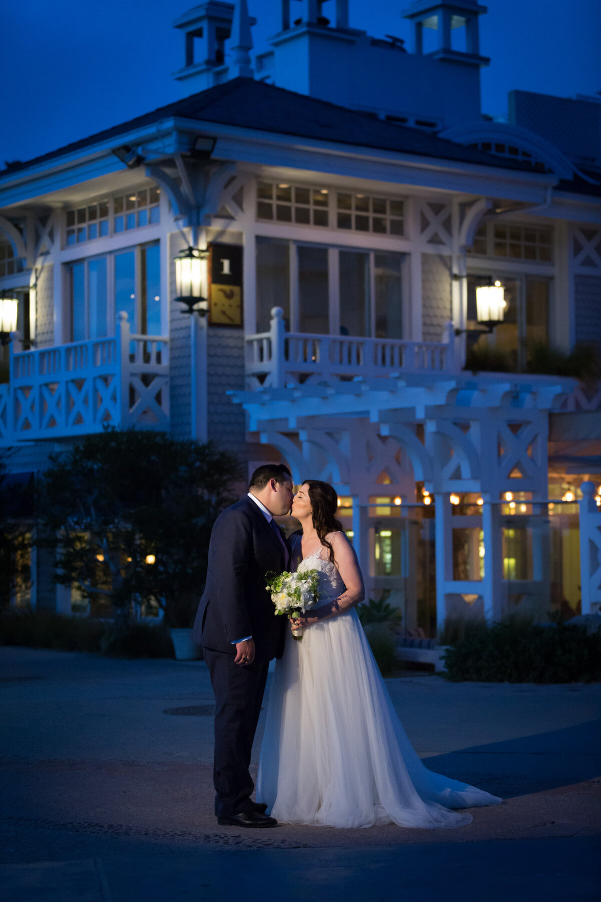 A bride and groom kissing while standing outside a large house