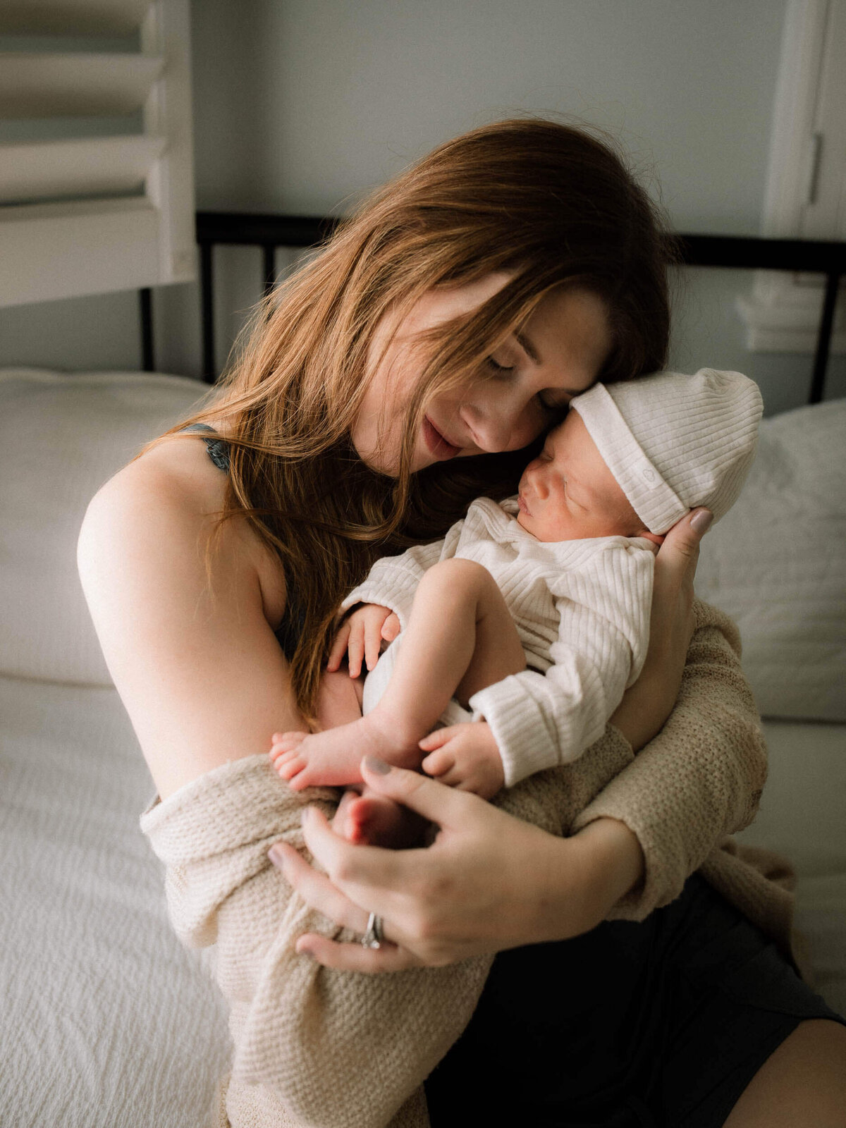Mom cradling her newborn son in the nursery, sitting on the bed, side lit by window light in Los Angeles home.