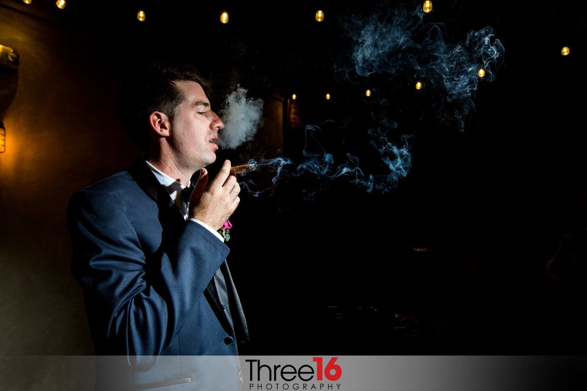 Groom takes a puff on a cigar in the evening