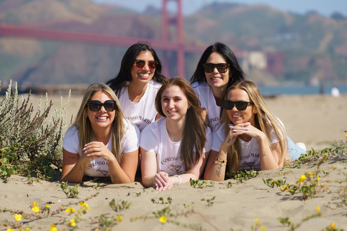 Five women laying on top of each other at the beach in front of the golden gate bridge