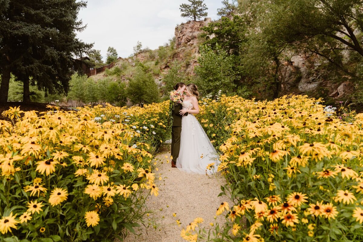 Lesbian couple kissing in a vibrant field of yellow wildflowers during their Lyons Colorado elopement, captured by Alpine Vows, a Colorado elopement photographer.