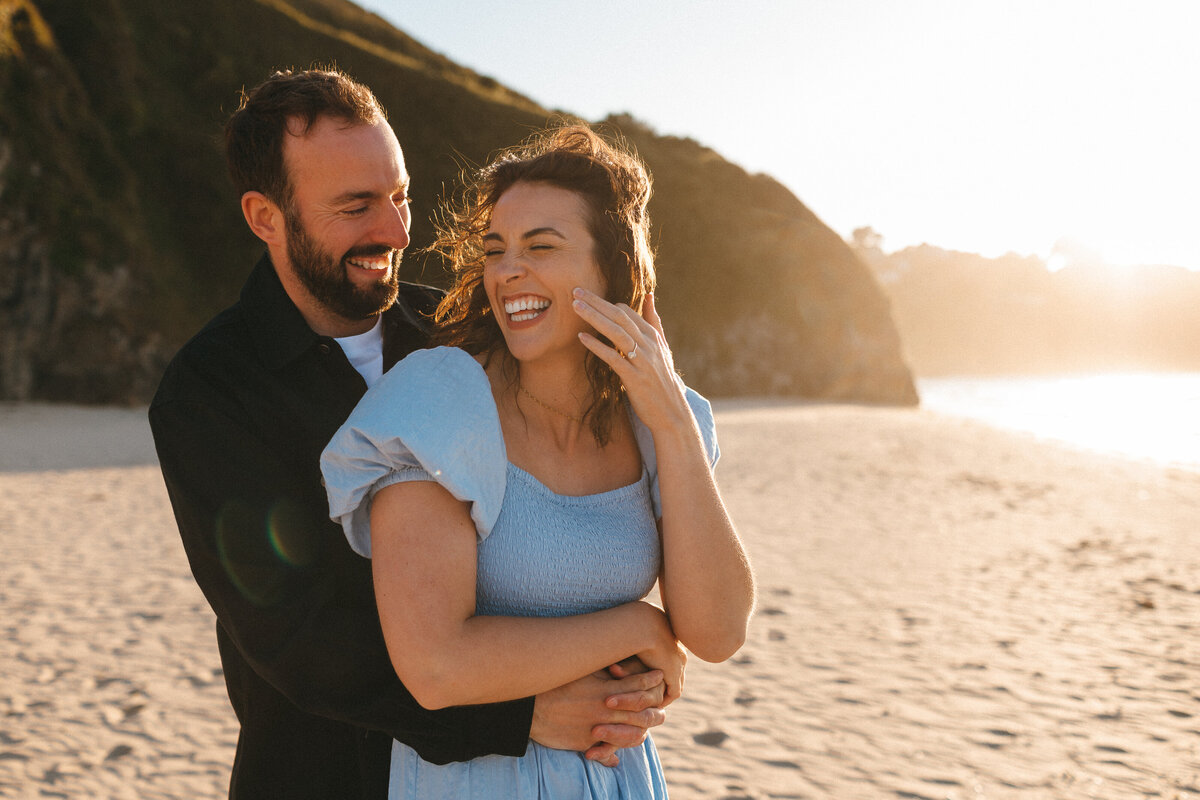 Photograph of a young  engaged couple laughing together  at the beach in West Cornwall on a sunny day