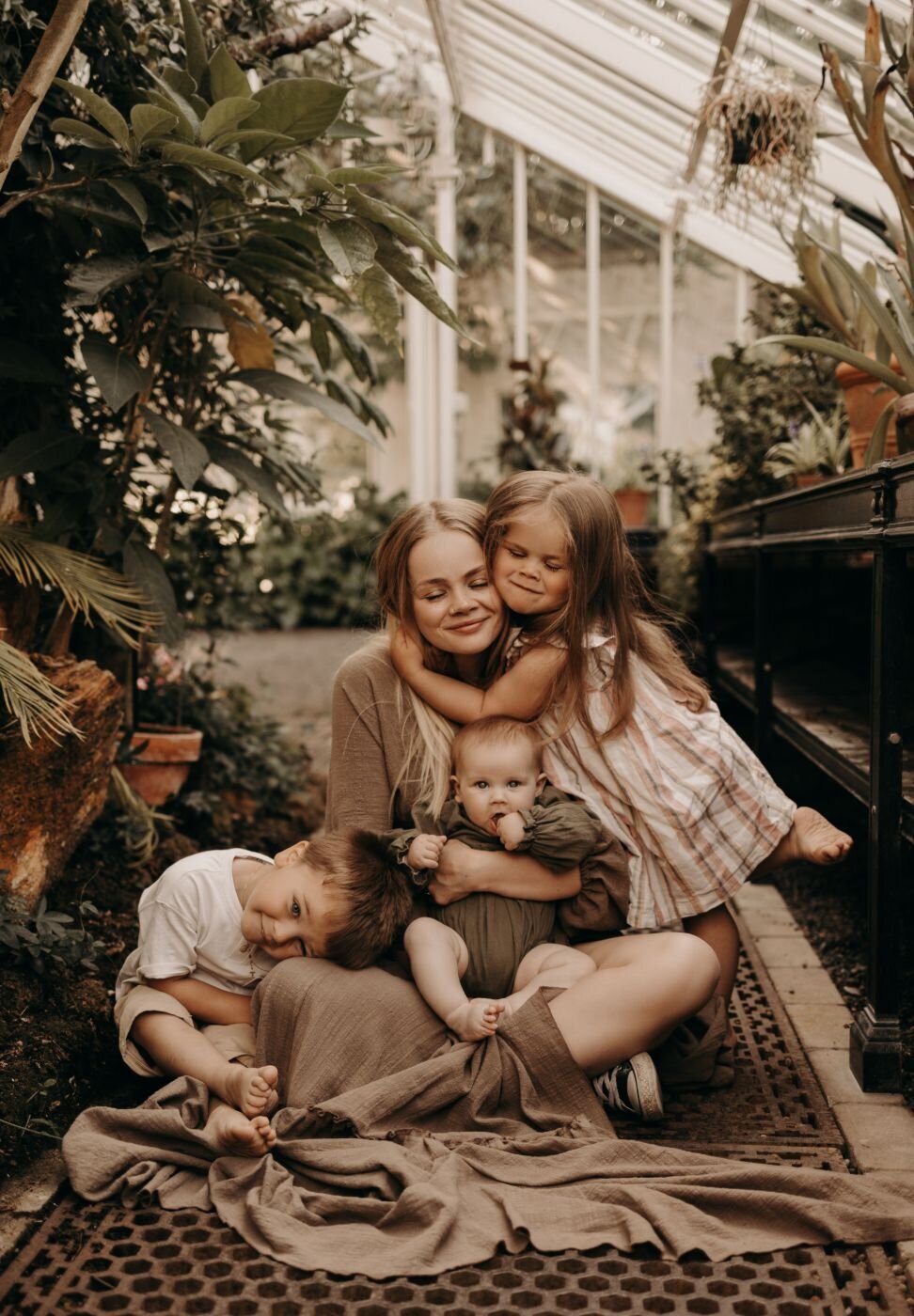 Mother embracing her three young children in a greenhouse setting during a Mullingar family shoot
