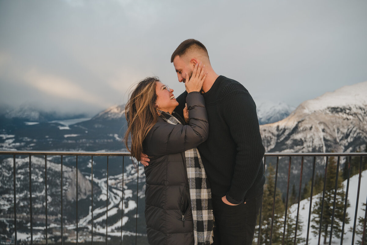 Couple reacts with joy to a winter proposal on a mountain viewpoint in Banff.