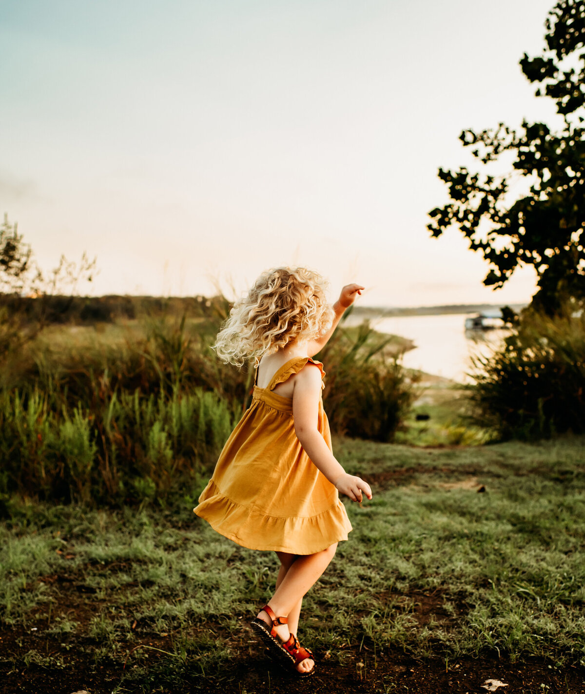 Little girl in a yellow dress twirling in the grass.