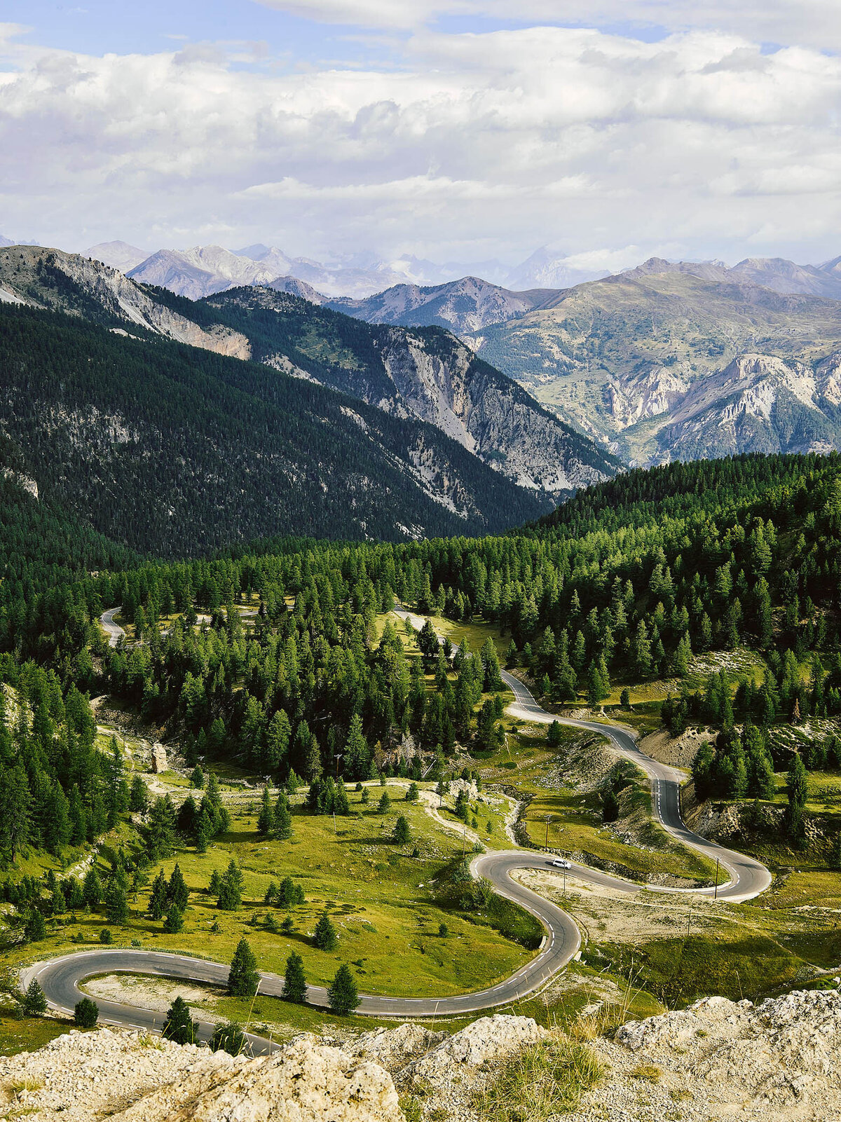 Serpentinenstraße durch einen dichten Nadelwald im Hochgebirge mit weiter Bergkulisse – professionelle Landschaftsfotografie für Werbung und Imagekampagnen