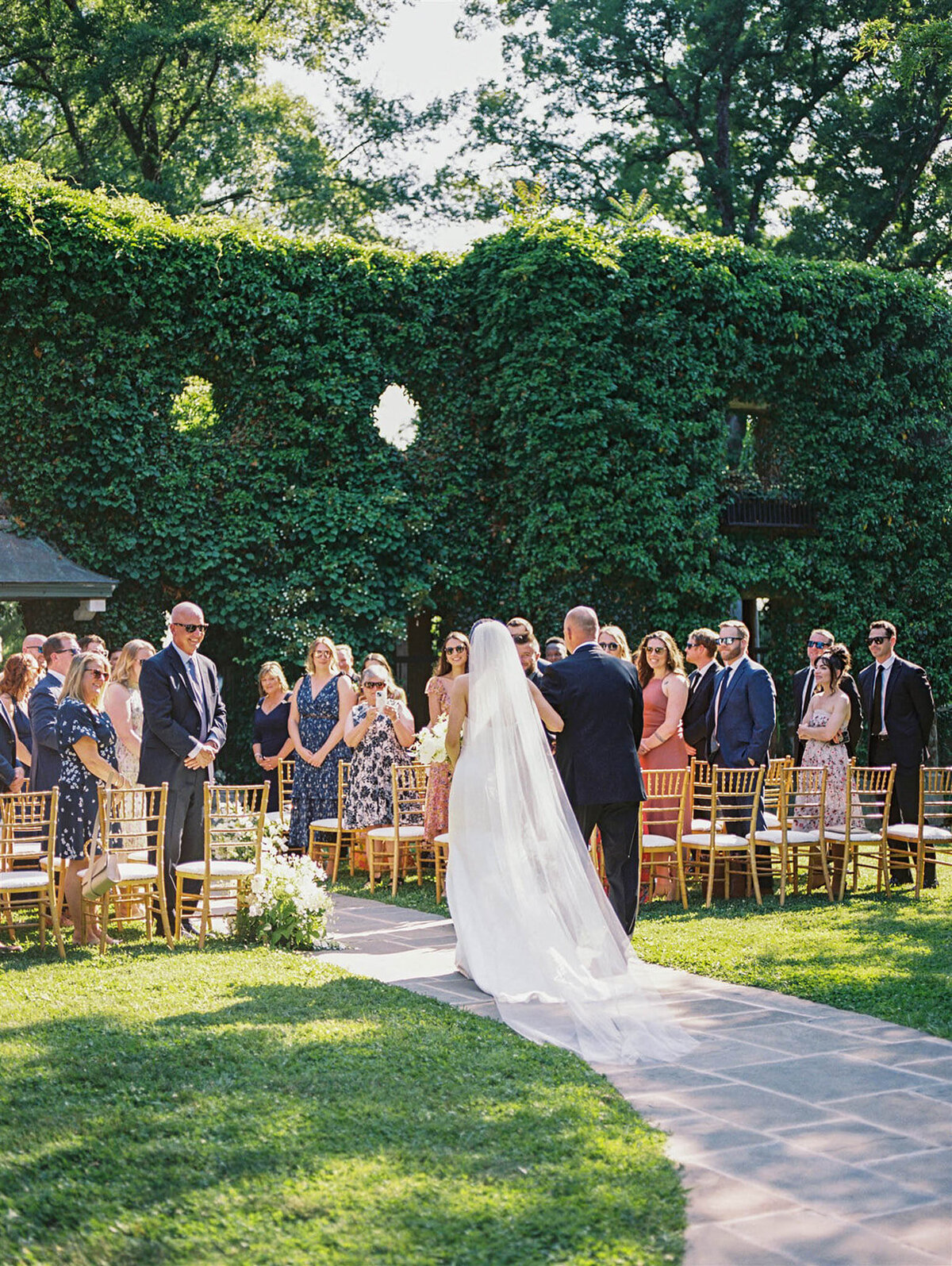 Bride walks down the aisle with her dad iby the ivy wall in Goodstone Inn