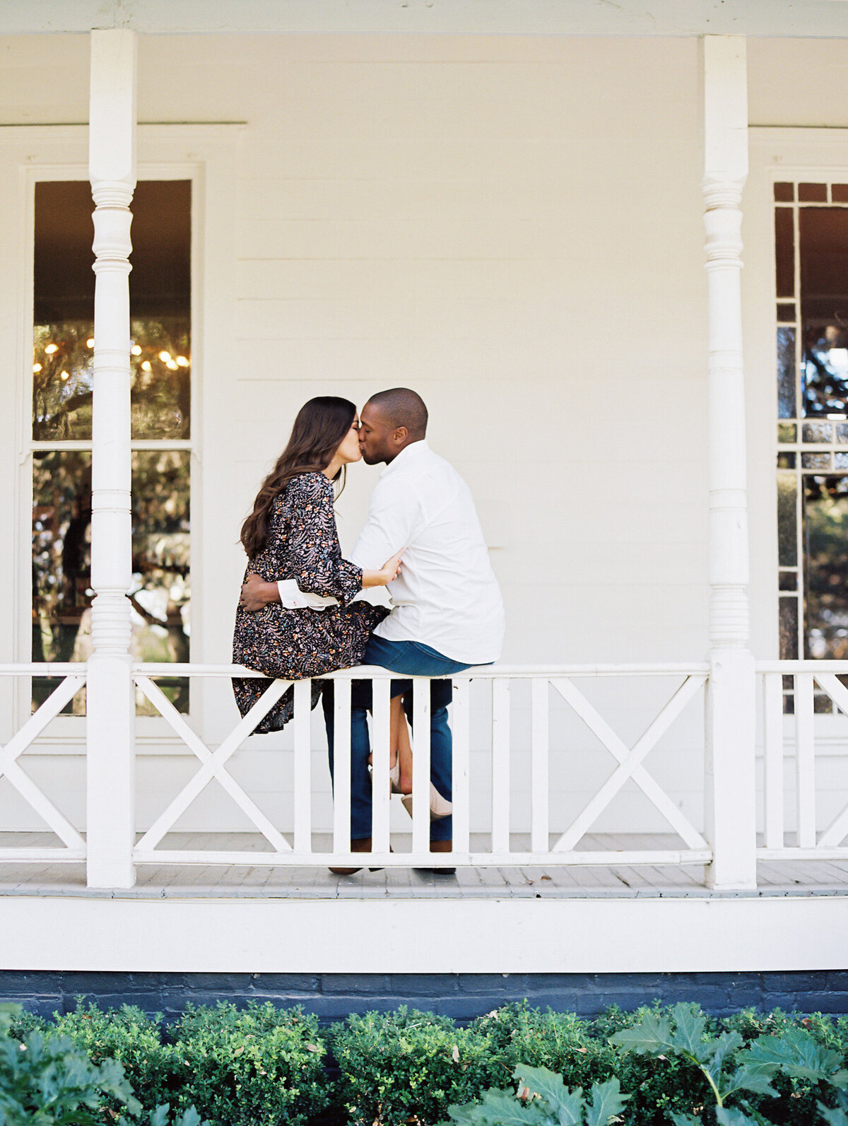 Couple kissing while sitting on a white porch railing