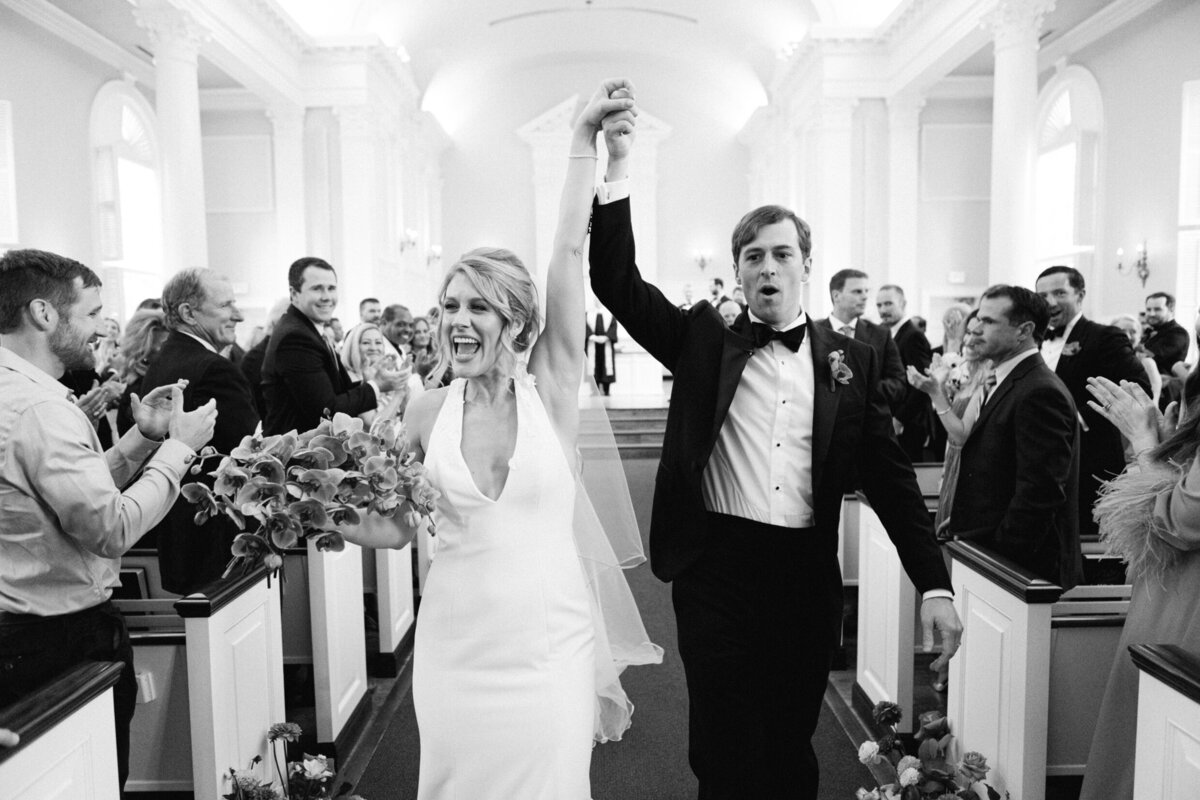 A wedding day black and white photo of the bride and groom walking down the isle celebrating after getting married