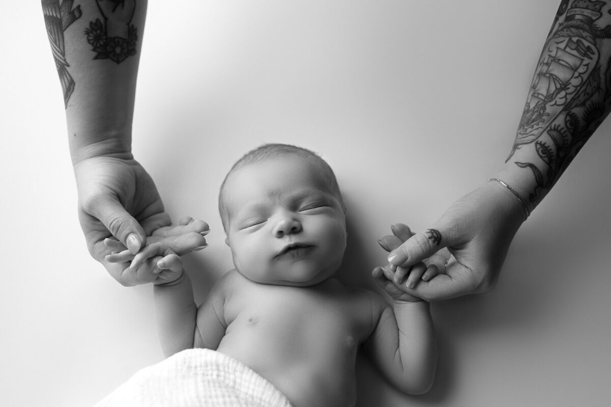 Studio newborn photo with baby holding tattooed hands of both parents | Timeless family newborn portrait near Leander and Austin
