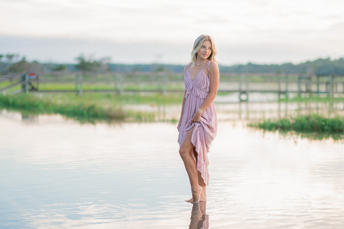 Teen girl in neutral-toned dress walking along the shore during her senior session at Kiawah Island beach