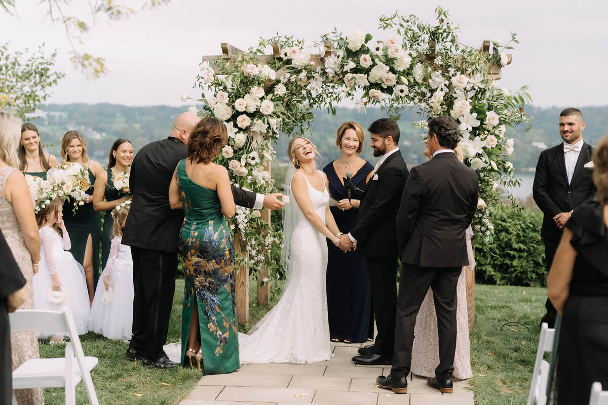 Wedding ceremony with floral arch, bride is laughing