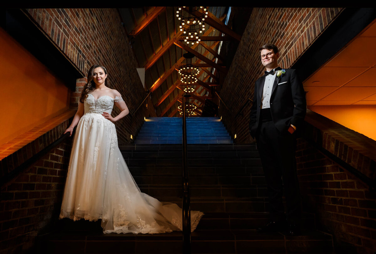 A bride and groom pose on the stairs in their wedding venue