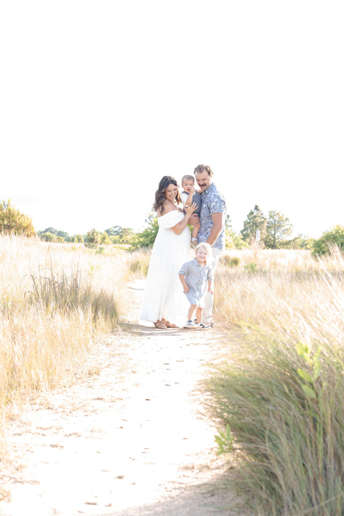 A Family stands snuggled up together on a beach trail by Virginia Beach Maternity Photographer Mary Eleanor Photography