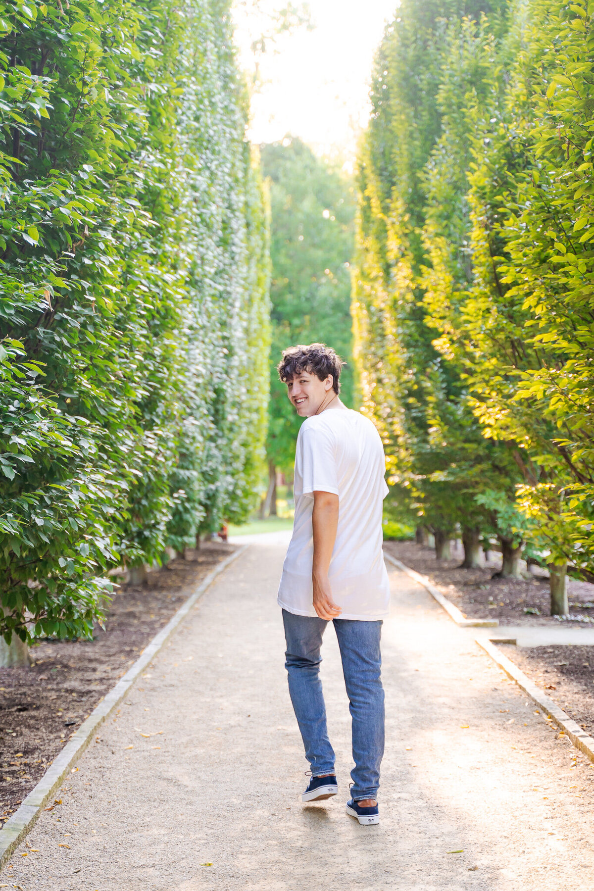 High school senior, Nic Allen, walks away and turns toward the camera with tall trees on both sides of him at the Franklin Park Conservatory in Columbus Ohio.