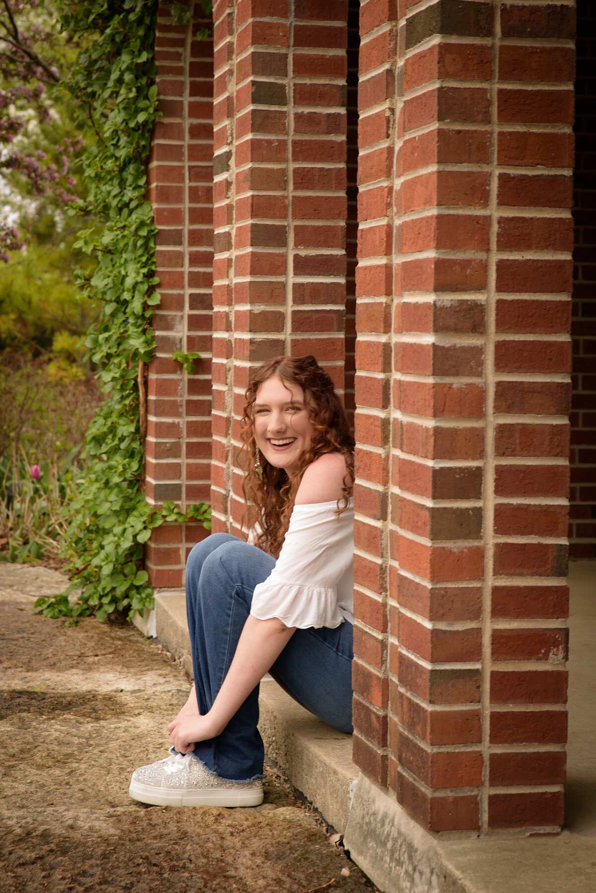 Green Bay East High School senior girl wearing a white sleeveless shirt and bell bottom jeans sitting behind a tulip garden in the red brick building at the Green Bay Botanical Gardens in Green Bay, Wisconsin.