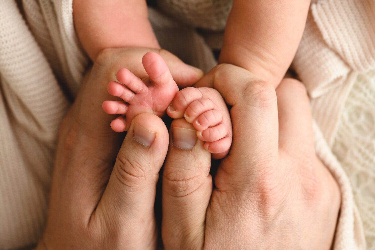 Close up image of tiny newborn toes being held in fathers large hands