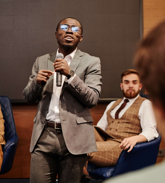 man speaking in front of panel at corporate event