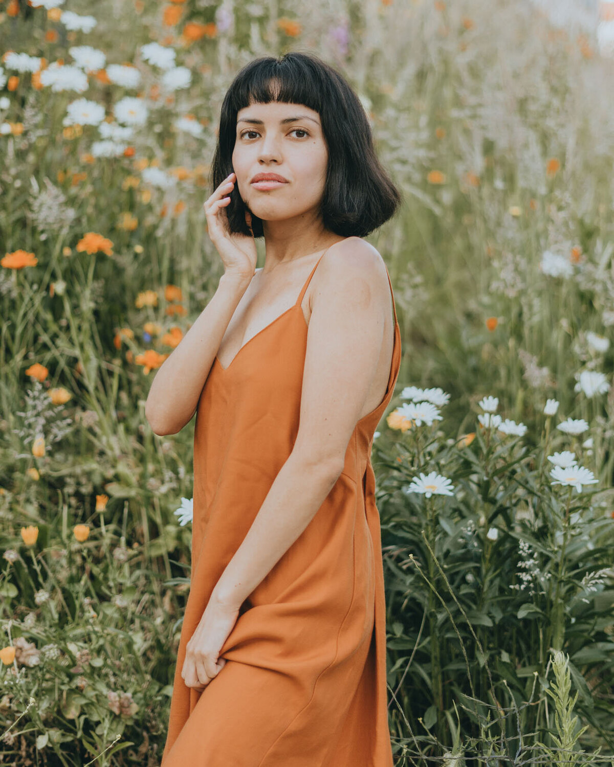 Girl in orange dress standing near a flower patch