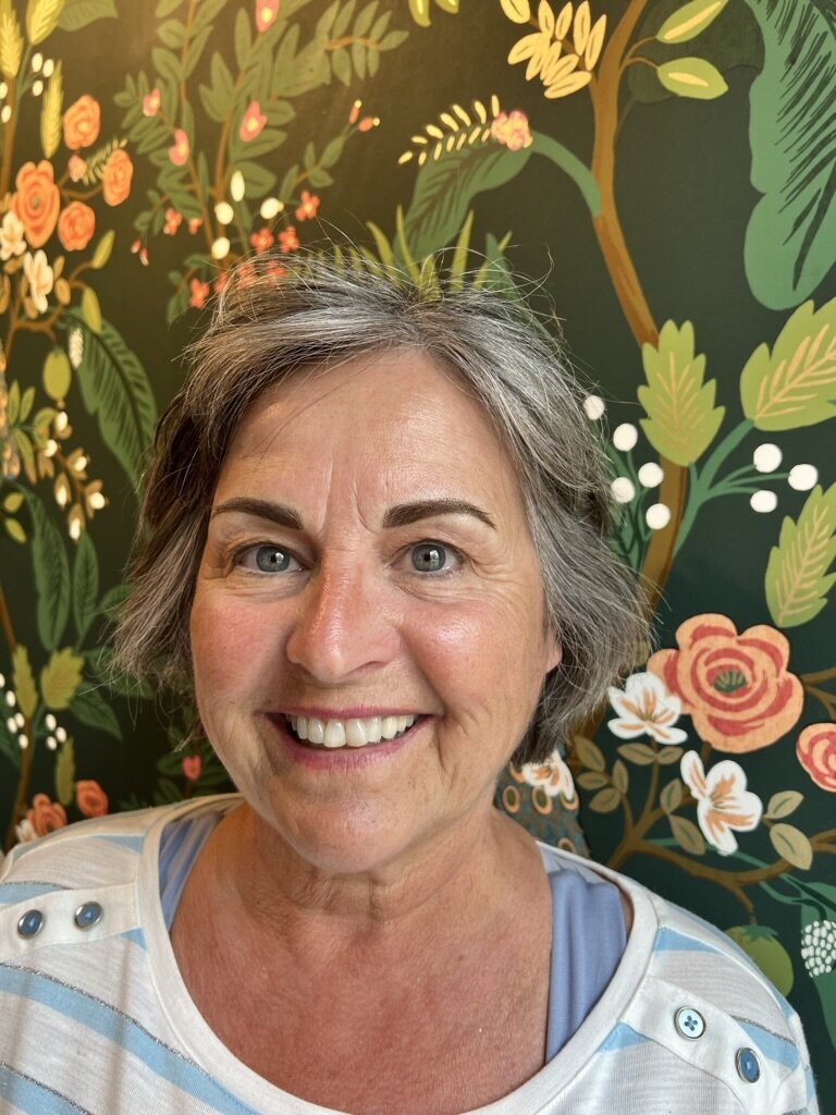 Woman with powder brows in front of floral wallpaper.