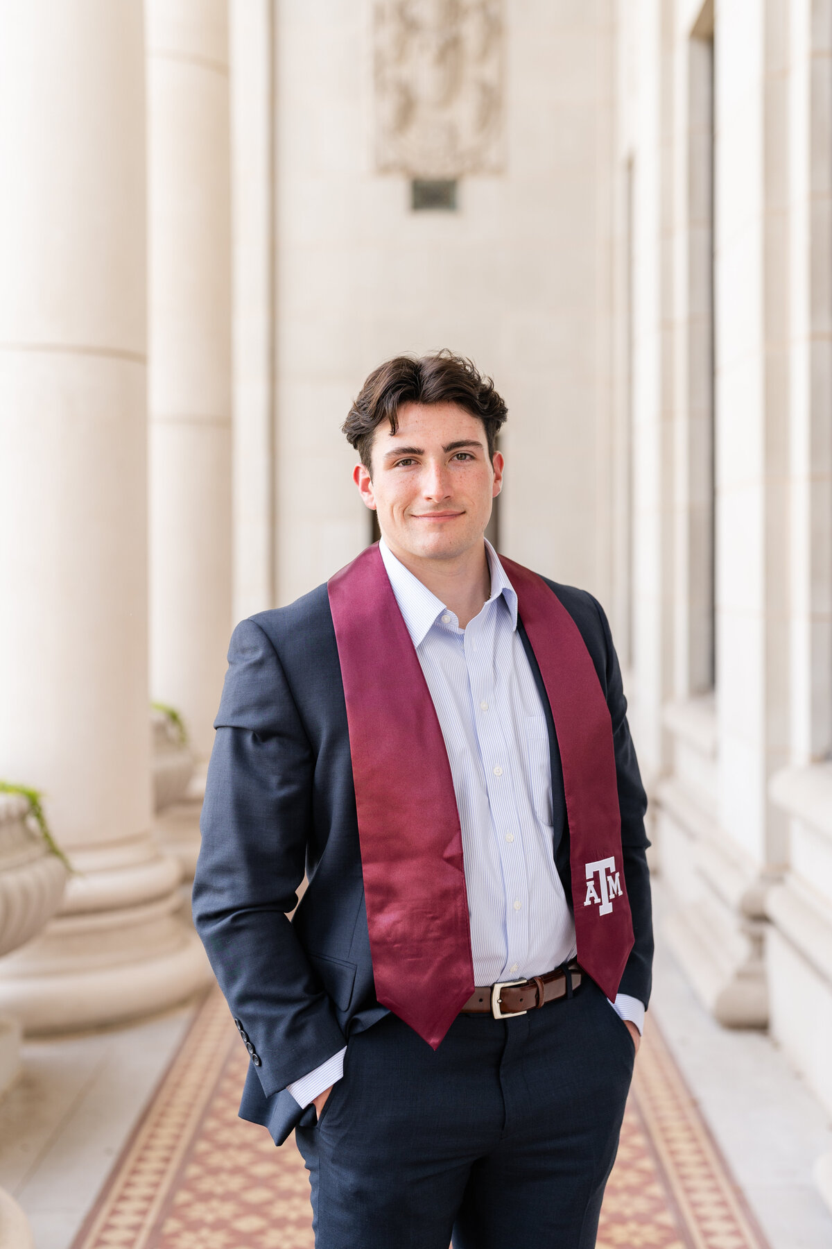Texas A&M senior guy standing with hands in pockets and wearing a suit with Aggie stole in columns at Administration Building